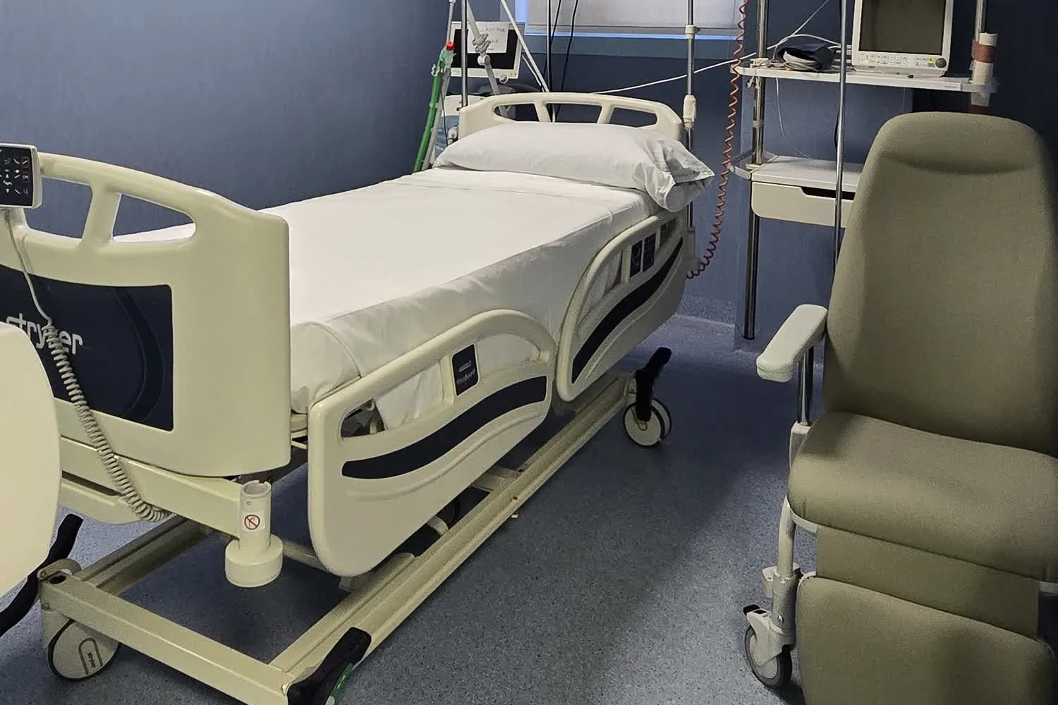 Box de intensivos preparado, con la cama articulada, el sillón del acompañante y el monitor en la cabecera