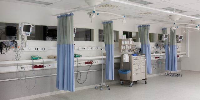 Sala de una unidad de cuidados intensivos vacía, con cortinas de separación y tomas de gases en la pared de cabecera